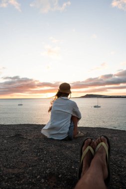 Sahilde bir kadının arka görüntüsü, sakin bir akşamda sakin bir günbatımını ve uzak bir tekneyi hayranlıkla seyrediyor..