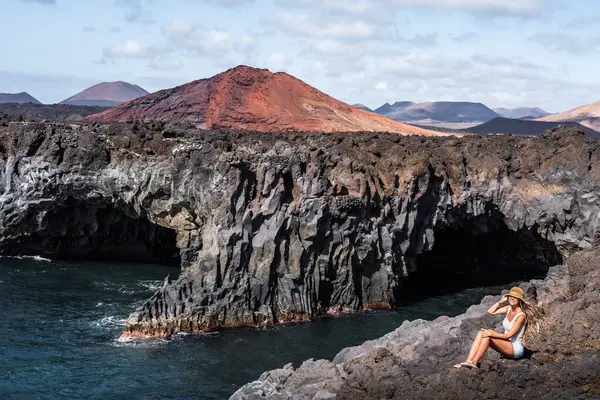 Bir kadın, Lanzarote 'deki Los Hervideros' ta şaşırtıcı volkanik kaya oluşumlarıyla çevrili okyanus kenarında huzurlu bir anın tadını çıkarır.