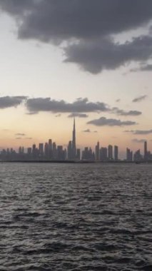 Gün batımında Dubais 'in ufuk çizgisinin uzak görüntüsü. Bulutlar yukarıda ve su renkleri yansıtıyor. Burç Halife