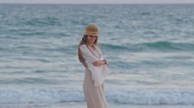 Güneş batarken kumlu sahilde gezinen bir kadın okyanus esintisinin ve sakin dalgaların tadını çıkarıyor..