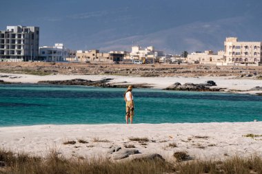 Kadın, Sur sahilindeki turkuaz suların ve şehir manzarasının tadını çıkarıyor, Umman.