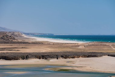 Çorak çöl manzarası, Umman 'ın güney kıyısı boyunca Arap denizinin turkuaz sularıyla birleşiyor.