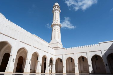 Müslüman bir kadın güneşli bir günde beyaz bir caminin avlusunda kemer ve minareyle namaz kılıyor.