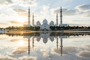 Şeyh zayed Büyük Cami 'nin gün batımında bulutlu gökyüzü ile suya yansıyan manzarası.