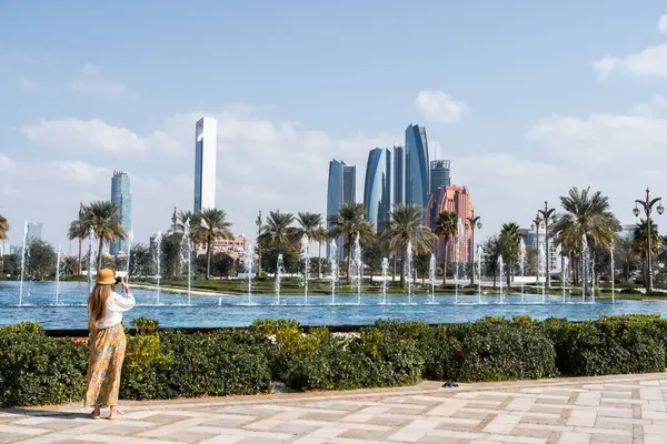 Abu Dabi 'nin etkileyici gökdelenlerinin, çeşmelerinin ve palmiye ağaçlarının resmini çeken bir turist.