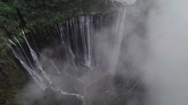Suyun drone görüntüsü Tumpak sewu şelalesine dalıyor, puslu bulutlar yaratıyor.