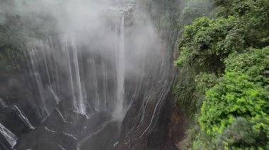 Drone 'un su manzarası Tumpak sewu şelalesinden, yemyeşil bitki örtüsüyle çevrili bir vadiye akıyor.