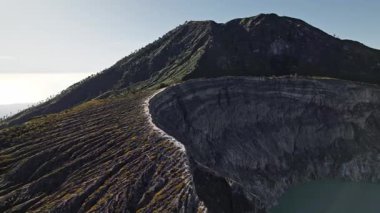 Yeşil yamaçlar karanlık volkanik kayalar ve turkuaz sülfür gölüyle gün doğumunda ijen Dağı kraterinde buluşur.