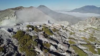 Kawah ijen Krateri Gölü üzerindeki sisli bir çift turist, turkuaz asitli su açığa çıkarıyor.