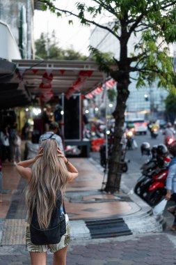 Sarışın turist, Asya 'nın güneydoğusundaki kalabalık caddede yürüyor ve saçlarını arkadan tutuyor.