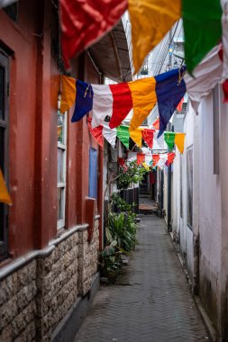 Dar bir sokakta sallanan Budist dua bayrakları canlı ve ruhani bir atmosfer yaratıyor.