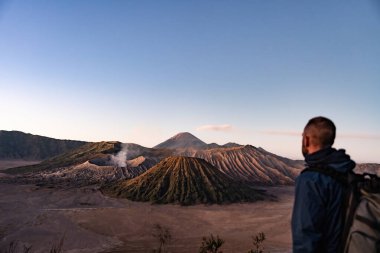 Sırt çantalı adam, tengger caldera 'nın tepesinde güneşin doğuşunu izliyor.