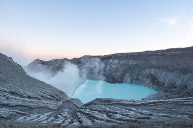 Kawah ijen volkan krateri şafak vakti turkuaz sülfür gölüyle sülfürik duman yayıyor.