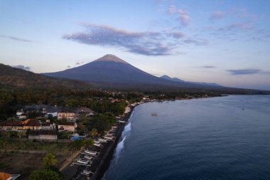 Gün doğumunda Agung Dağı 'nın görkemli varlığının altında kıyıda uzanan geleneksel balıkçı teknelerinin bulunduğu sakin sahil kasabası Bali' nin havadan görünüşü.
