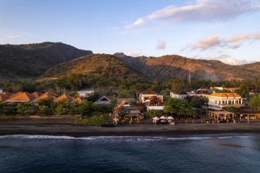 Büyüleyici gündoğumu, geleneksel evlerin ve tatil beldelerinin üzerine sıcak bir ışık saçıyor. Adı, bali, Endonezya 'nın siyah kumsalında.