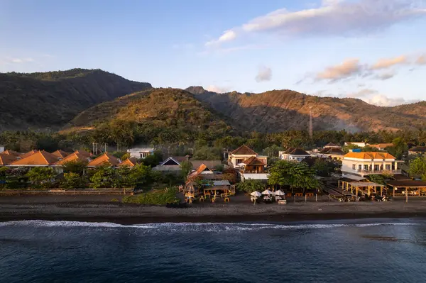 Büyüleyici gündoğumu, geleneksel evlerin ve tatil beldelerinin üzerine sıcak bir ışık saçıyor. Adı, bali, Endonezya 'nın siyah kumsalında.