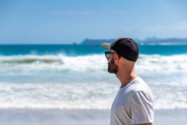 Güneş gözlüğü ve şapka takan turist güneşli bir günde deniz manzarasının tadını çıkarıyor.