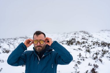 Yürüyüşçü kış macerasında karlı dağ manzarasının keyfini çıkarırken güneş gözlüğünü ayarlıyor