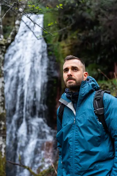 Erkek yürüyüşçü ormanda bir şelale manzarasının keyfini çıkarıyor.
