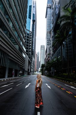 Singapur 'un finans bölgesinde boş bir caddenin ortasında yürüyen sarışın turist gökdelenlere hayran.
