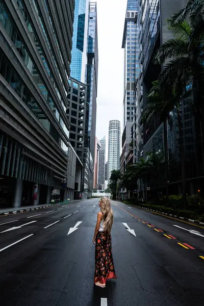 Singapur 'un finans bölgesinde boş bir caddenin ortasında yürüyen sarışın turist gökdelenlere hayran.