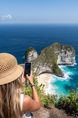 Sarışın turist, Nusa Penida, Bali 'deki ünlü Kelingking plajının fotoğrafını çekiyor.