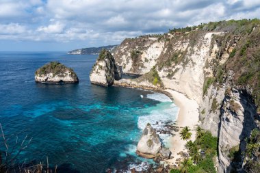 Elmas plajı, Nusa Penida, baş döndürücü beyaz uçurumlar, turkuaz su ve bulutlu bir gökyüzünün altında resim gibi bir manzara.