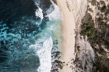 Tenha bir kumsala çarpan turkuaz dalgaların nefes kesen hava manzarası dramatik bir uçurumun kenarına kurulmuş, muhteşem bir kıyı manzarası yaratıyor.