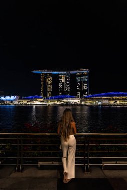 Singapur 'daki marina Bay Sands Oteli' nin göz kamaştırıcı gece manzarasının tadını çıkaran genç bir kadın.
