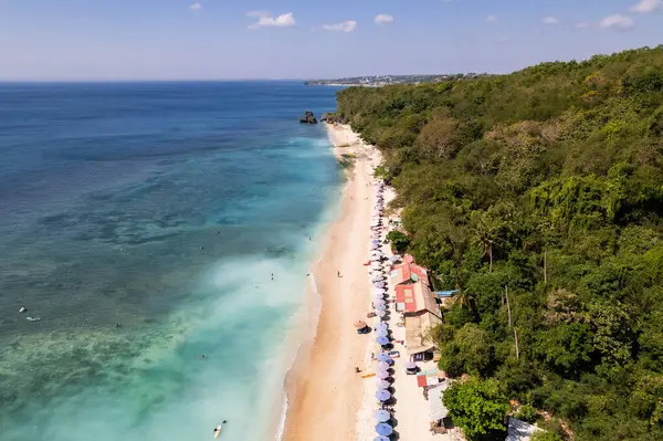 Bali, Endonezya 'da güzel bir tropik sahil manzarası, turkuaz su, plaj şemsiyeleri ve yemyeşil bitki örtüsünü gösteriyor.