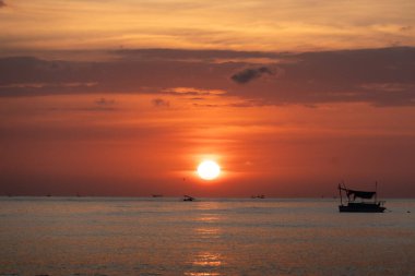 Bali 'deki sakin okyanusun üzerinde canlı bir günbatımına karşı siluet oluşturan balıkçı teknelerinin sakin manzarası.