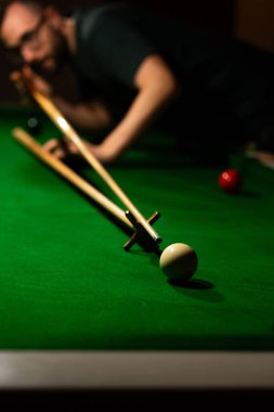 Odaklanamayan Snooker oyuncusu, yeşil bir bilardo masasında beyaz topu hedeflemek için dinleniyor.