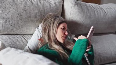 Genç bir kadın rahat bir koltukta dinlenirken akıllı telefon kullanıyor.