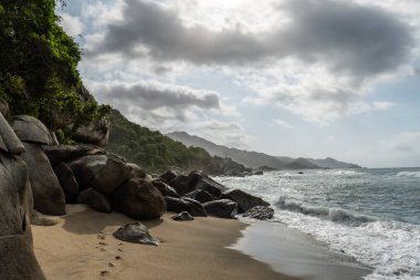 Okyanus dalgaları, Tayrona Ulusal Parkı, Kolombiya 'da kayalar ve ormanlarla dolu güzel bir plajın kıyısına çarpıyor.
