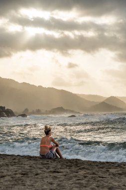 Günbatımında Kolombiya sahillerinde dinlenen bir turist okyanus dalgalarına hayran.