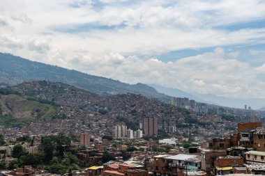 Medellin, Kolombiya 'daki Favela dağları tuğla evler, yüksek binalar ve bulutlu gökyüzünün altındaki yeşil ağaçlarla genişletiyor.