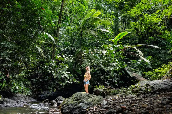 Kolombiya yağmur ormanlarının yemyeşil bitkilerinin ve taze akıntısının tadını çıkaran genç bir kadın doğanın güzelliğini kucaklıyor.