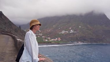 Gülümseyen kadın, La Gomera adasındaki bir kıyı köyünün ve okyanusun manzarasına hayran.