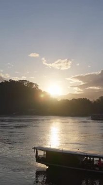 Golden sun reflecting on the mekong river with a traditional wooden tour boat floating peacefully
