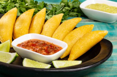 Tahta arka planda baharatlı sos ve guacamole soslu Kolombiya Empanadası.