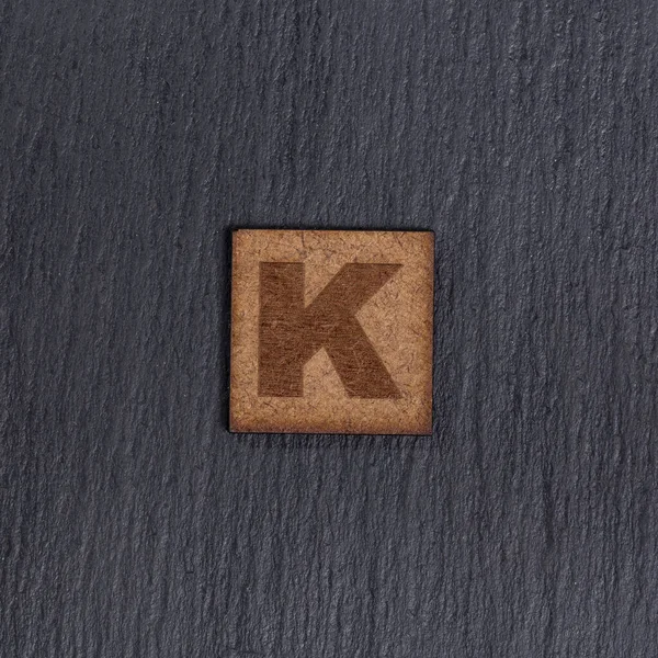 正方形の木製のタイルで大文字 手紙K 黒の石の背景に — ストック写真
