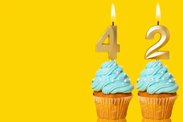 Geburtstag Cupcakes Mit Kerzen Lit Forming Number Foto Auf Gelbem lizenzfreie Stockbilder