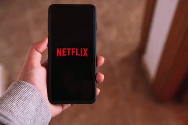 MLAGA - İspanya - 6 Nisan 2023: akıllı telefondan Netflix 'i yayınlayan kadın. Dijital cihazlar. Uygulama telefonu. Netflix ve soğutma.
