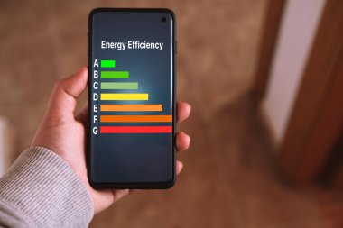 Kadının eli ekranda enerji verimliliği etiketli bir akıllı telefonu tutuyor. Düşük tüketim ve verimli ürünler. Karbon ayak izini azalt. Yeşil çevre dostu iş. Düşük CO2 emisyonları.