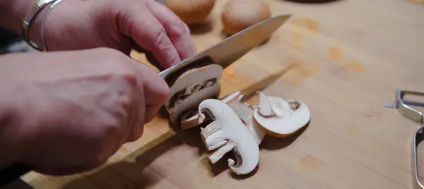 キッチンボードに新鮮なキノコを切る手のクローズアップ 健康的な食べ物を調理する — ストック写真