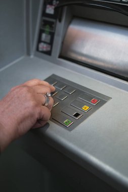 Orta yaşlı bir kadın bankamatiği kullanıyor. Şifre defterinde PIN güvenliğine basıyor..