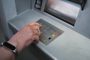 Orta yaşlı bir kadın bankamatiği kullanıyor. Şifre defterinde PIN güvenliğine basıyor..