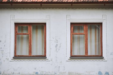 Beyaz yıpranmış bir duvardaki iki kahverengi ahşap pencerenin yakın çekimi. İki ahşap pencereli eski tarz bir evin parçası.