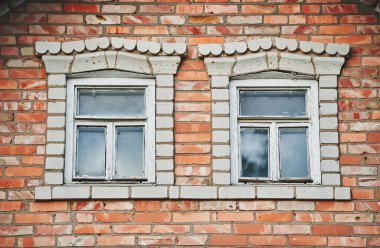 Kırmızı tuğlalı bir duvarda camda gökyüzü yansıması olan iki klasik ahşap pencere. Tarihi bir tuğla evin ön cephesinin bir parçası. Çatının altındaki ikinci kattaki pencereler.