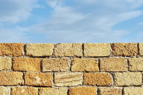 stock image Old yellow wall made of natural stone blocks. Shell stone wall of an ancient building against the sky